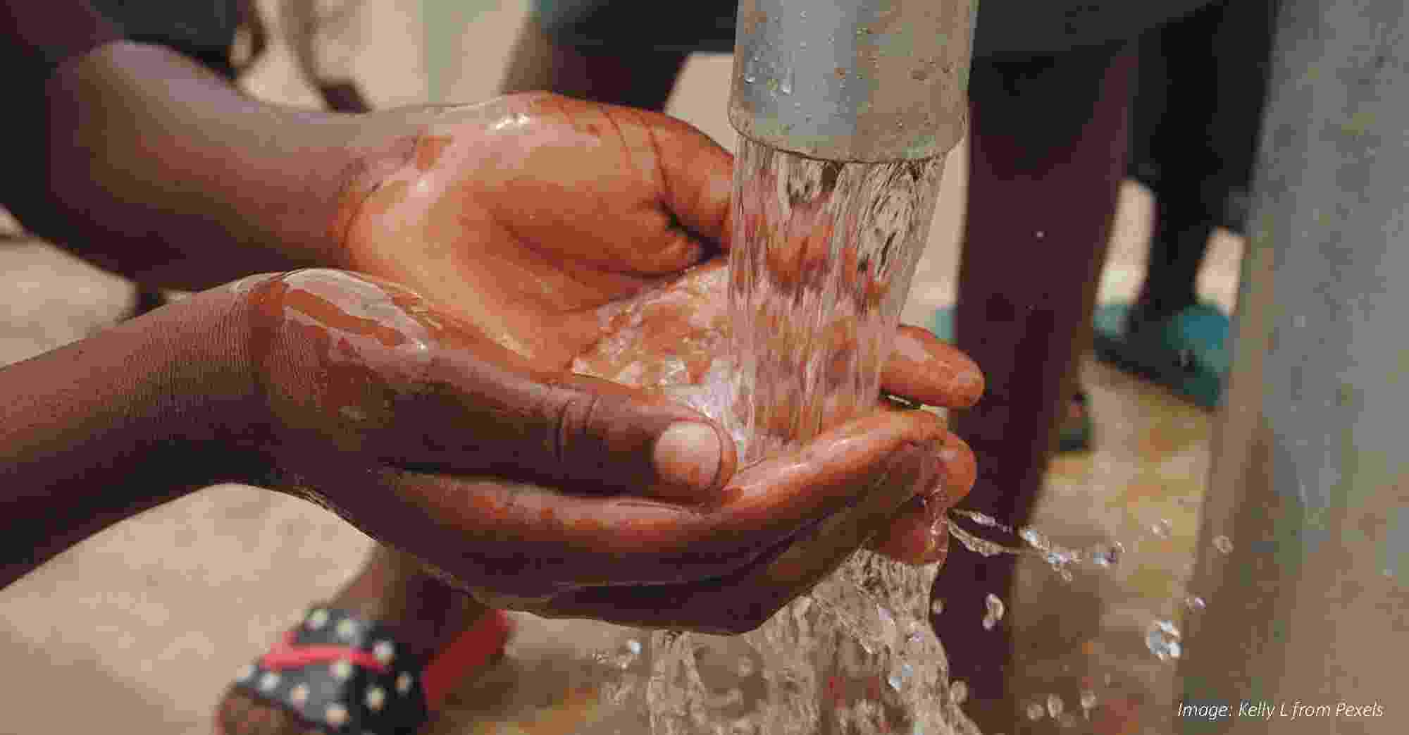 Image shows a child holding their hands under clean water flowing out of a pipe